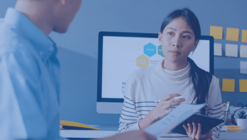 A man and woman discuss critical flaws in the QA process while seated in front of a computer.